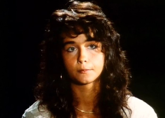 Young woman with dark curly hair and blue eyes in a dimly lit setting related to Vatican Girl cold case mystery.
