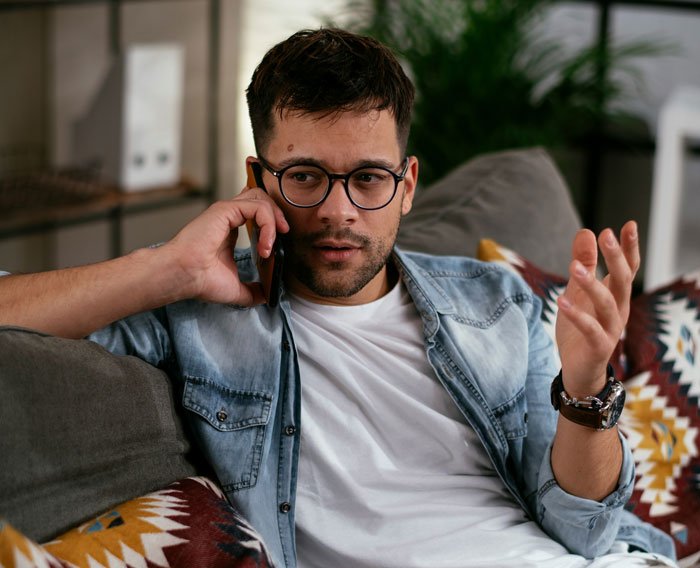 Man in casual clothes talking on phone at home, discussing gym time and babysitting arrangements.