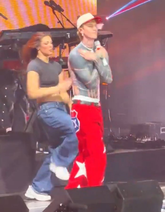 Machine Gun Kelly dancing on stage with a female dancer in casual and colorful outfits during a live performance.