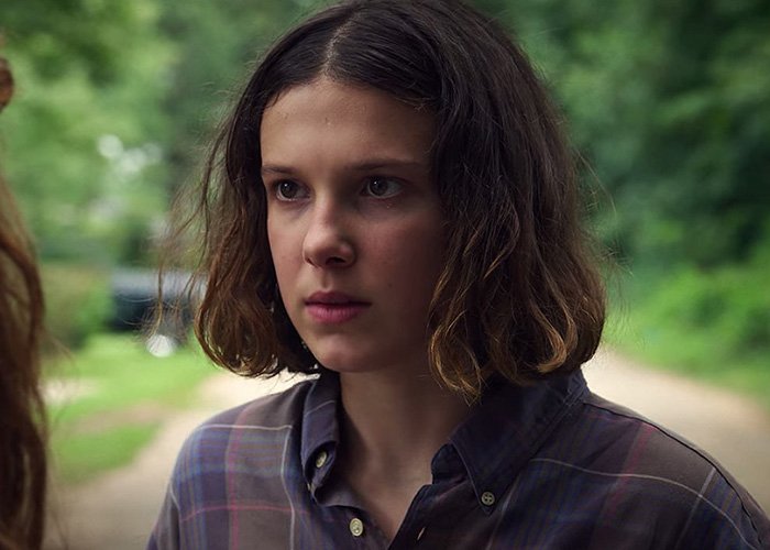 Millie Bobby Brown in a plaid shirt outdoors, focused expression, key character in popular Stranger Things series.