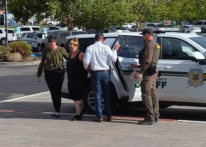 Woman being escorted by law enforcement officers near a sheriff’s vehicle after being charged in 5-year-old daughter’s slaying.
