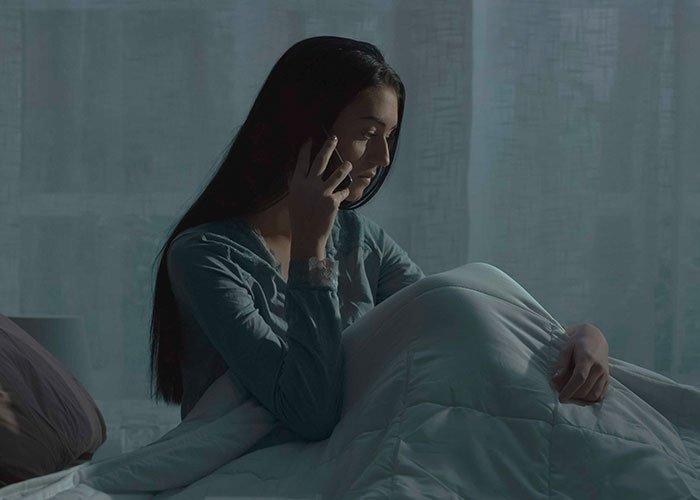 Woman on phone, sitting on bed at night, reflecting on her relationship after being ditched with a newborn by boyfriend.