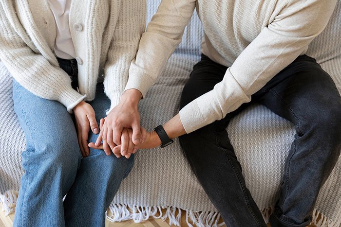 Couple sitting on couch holding hands, illustrating a guy going above and beyond for his ex girlfriend.