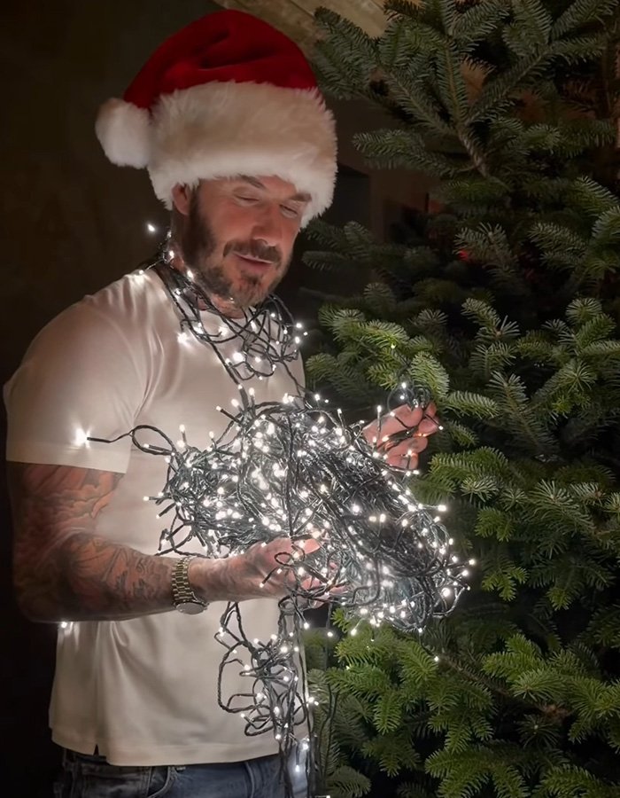 Man wearing Santa hat holding tangled Christmas lights near a tree, related to Brooklyn’s wife Nicola Peltz and Victoria posts.