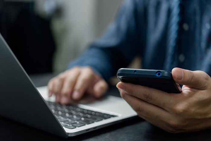 Man holding phone and typing on laptop, illustrating heroic Texas dad tracking kidnapped daughter’s phone.