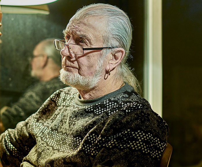 Elderly man with glasses and earring looking pensive, reflecting on guy kicking siblings out after surprise reveal.