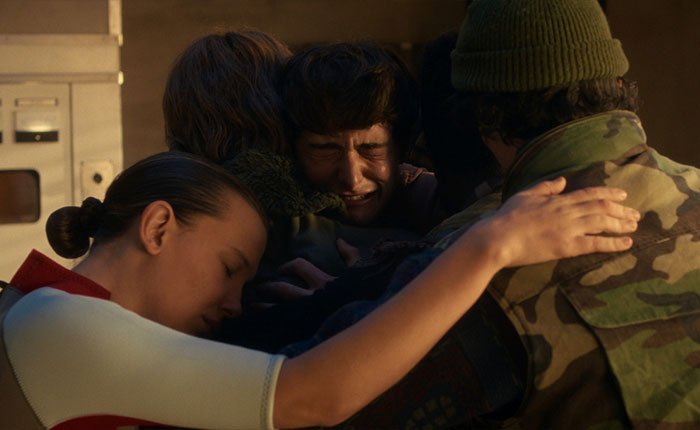 Stranger Things 5 cast in emotional group hug scene, highlighting the comically bad reaction to the latest episode online.