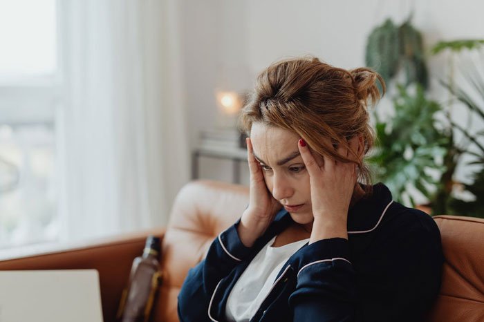 Woman sad and stressed sitting on couch, holding her head, reflecting on ending a long friendship after tough request