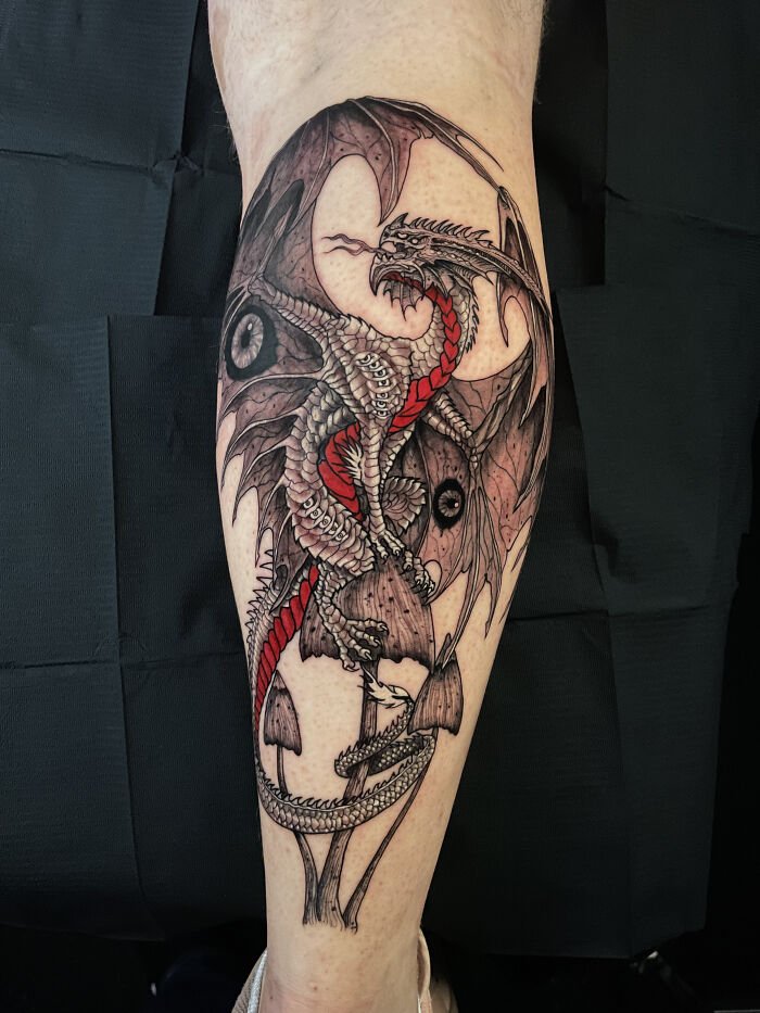 Psychedelic tattoo of a detailed dragon with red accents wrapped around mushrooms on a person’s leg.