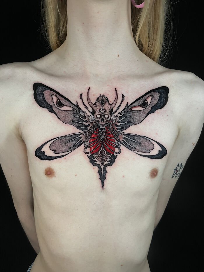 Chest tattoo of a surreal insect with eyes on its wings and skeletal red heart, showcasing psychedelic tattoos art style.