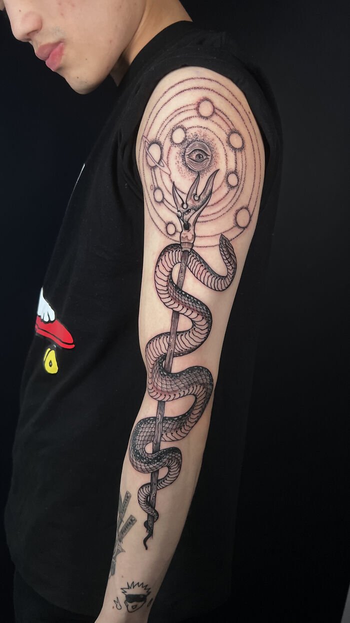 Person showing a detailed psychedelic tattoo featuring a snake, cosmic symbols, and an all-seeing eye on the upper arm.