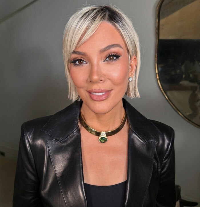Woman with short blonde hair wearing a black leather jacket and gold necklace, representing viral facelift and hands never lie concept.