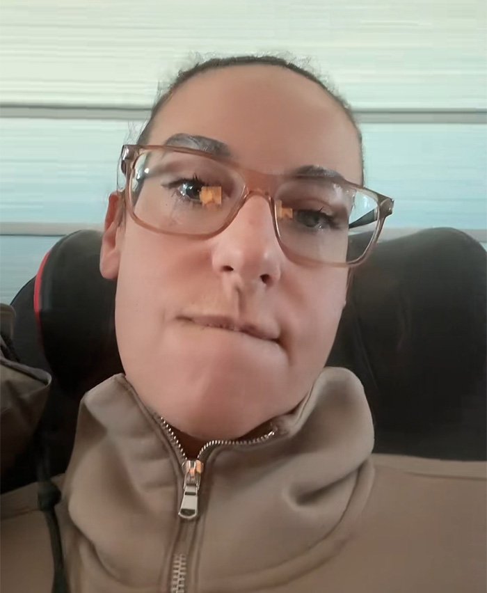 Woman with glasses and beige jacket expressing frustration on an Air Canada flight about an expired meal issue.