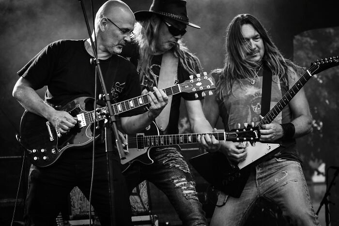 Three musicians playing electric guitars on stage, performing classic rock tracks in a lively concert setting.