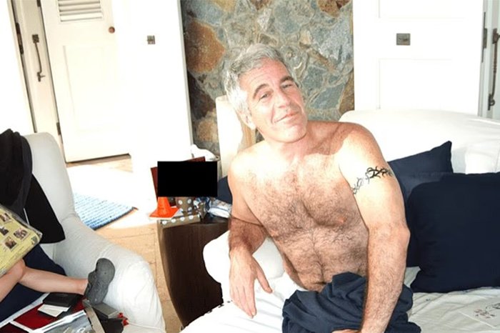 Man with tattoo sitting shirtless on a white couch as a toddler's foot appears beside Epstein in a photo.
