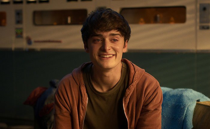 Young man in casual hoodie smiling indoors, representing Stranger Things 5 characters in a scene from the series.