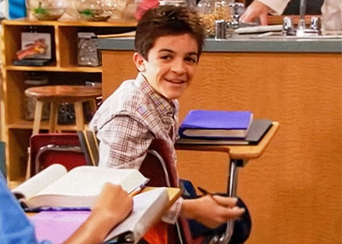 Young boy sitting in classroom, smiling and holding a pen, related to dad of Nickelodeon star Tylor Chase health update.