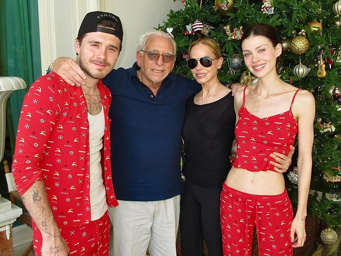 Brooklyn’s wife Nicola Peltz and Victoria pose in festive attire by a decorated Christmas tree during holiday celebrations.