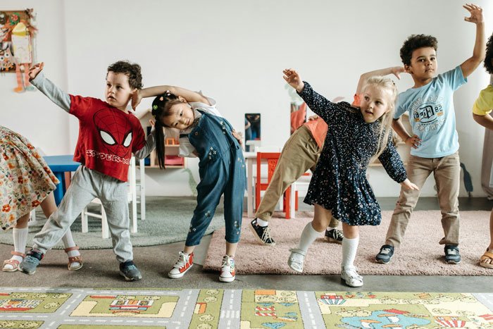 Young children stretching and playing in daycare, highlighting challenges faced by a jobless wife and busy husband.