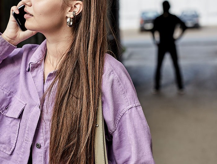Woman making phone call in foreground with shadowy man in background symbolizing heroic Texas dad tracking phone.