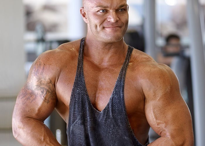 Muscular man in a gym wearing a tank top, representing strength and tension related to risking future child&rsquo;s health.