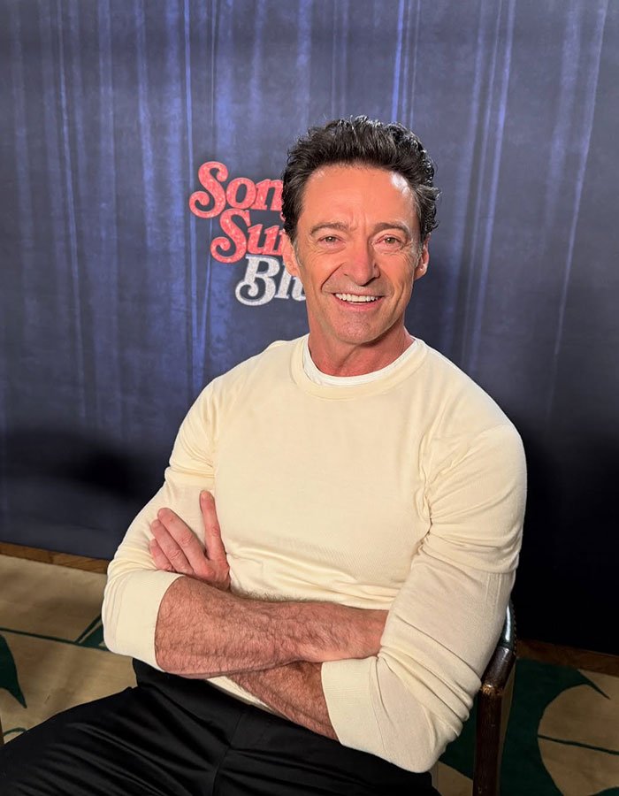 Hugh Jackman smiling in a cream long sleeve shirt during an indoor event amid divorce controversy.
