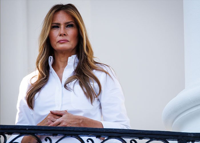 Melania Trump standing on a balcony wearing a white shirt, related to discussions about her new documentary.