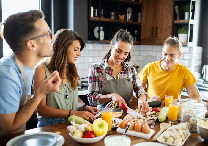 Family cooking together in a kitchen with a husband, woman, and others preparing food for a picky eater with allergies.