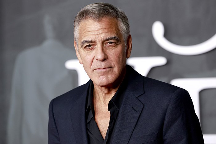 George Clooney in a dark suit, posing solemnly at an event, sharing heartfelt tribute after sister's passing.