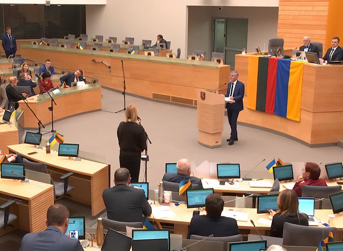 Lithuanian parliament session with lawmakers discussing new law involving lawmaker’s cat and broadcaster head firing.