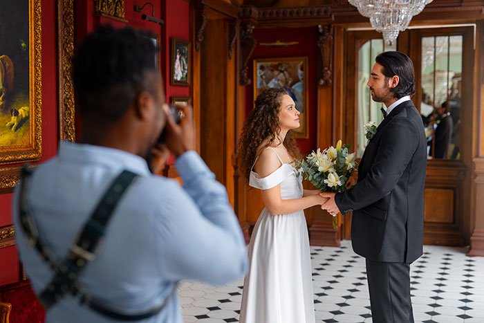 Bride and groom standing together while a photographer captures wedding photos in an elegant room with red walls.