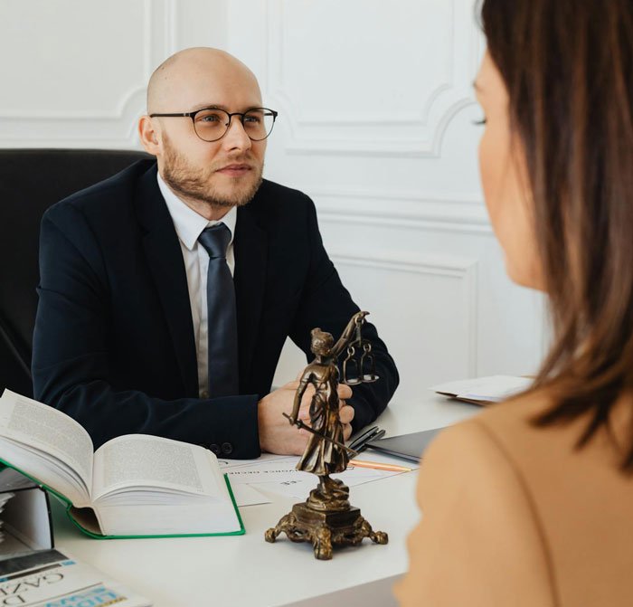 Man consulting with lawyer about divorce, legal books open, Lady Justice statue on desk in a professional office setting.