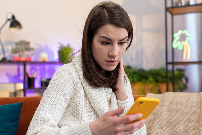 Young woman in white sweater looking upset while holding a yellow phone, reflecting anger over TikTok fame lies about sister.
