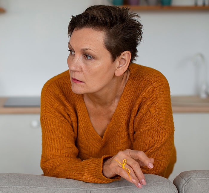 Woman in orange sweater looking concerned, illustrating a mom accused of embarrassing son’s girlfriend in a home setting.