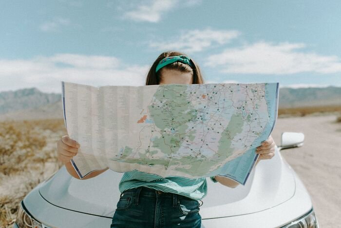 Person holding a map while leaning against a car in a desert landscape, testing geography knowledge and map mistakes.