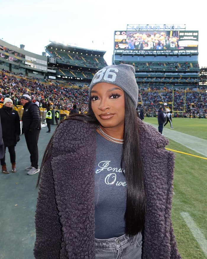 Simone Biles at stadium wearing gray beanie and coat, amid crowd, linked to controversy over dog with chopped-off ears.