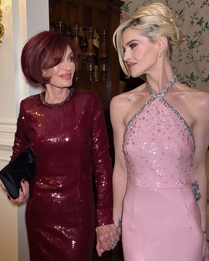 Sharon Osbourne and Kelly Osbourne holding hands, dressed in elegant sequined gowns at an event.