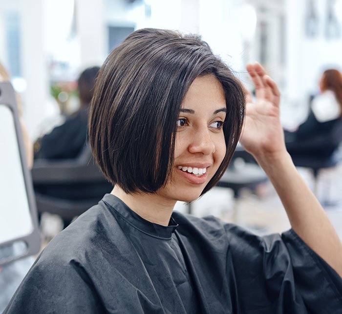 Young woman with a new hairstyle smiling in a salon representing Gen Z redefining rude Millennial women trends.