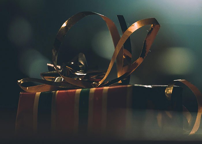 Wrapped Angel Tree gift with gold ribbon in low light, symbolizing mom filming son’s reaction and gift ungratefulness.