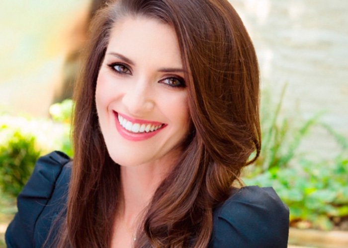 Smiling woman with long brown hair and black top outdoors, representing publicist quitting Meghan Markle and Prince Harry team.