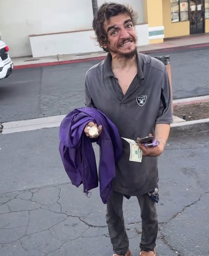 Man holding a purple jacket and cash on a c*****d street, related to Tylor Chase’s hospitalization aftermath and friend’s revelation.