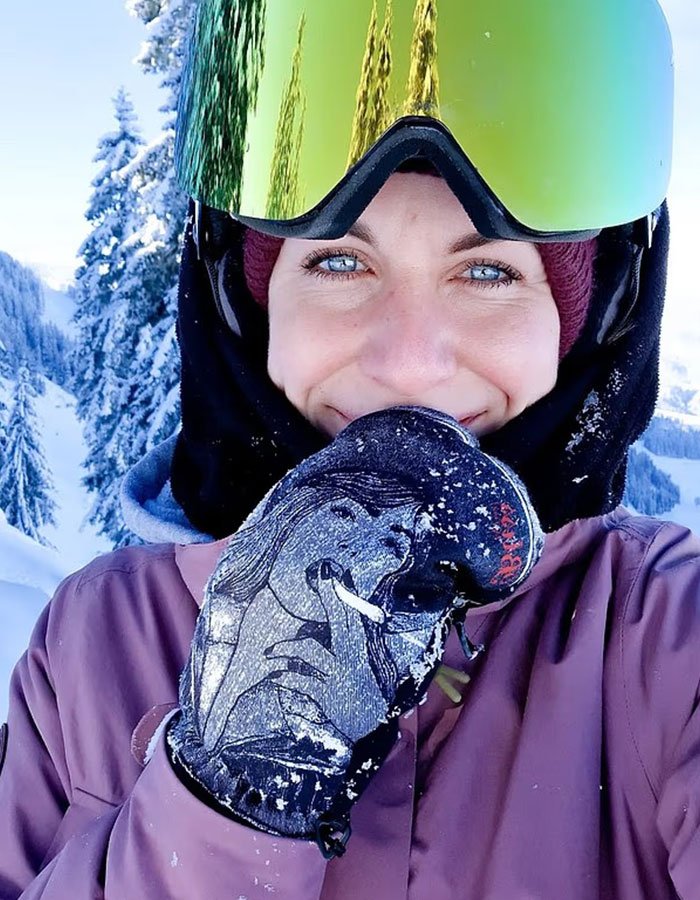 Young woman smiling in ski gear on a snowy mountain, related to woman abandoned to fatally freeze on Austria’s peak.