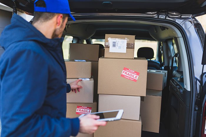 Delivery driver checking fragile packages in the back of a van related to woman’s shattered Christmas gift claim.