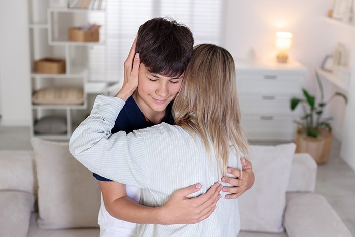 Woman hugging her nephew in living room as nephew calls her mom, causing tension with his bio mom.