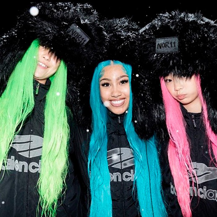 Three women wearing colorful wigs and black fur hats, styled fashionably amid winter snowfall, in a bold group look.