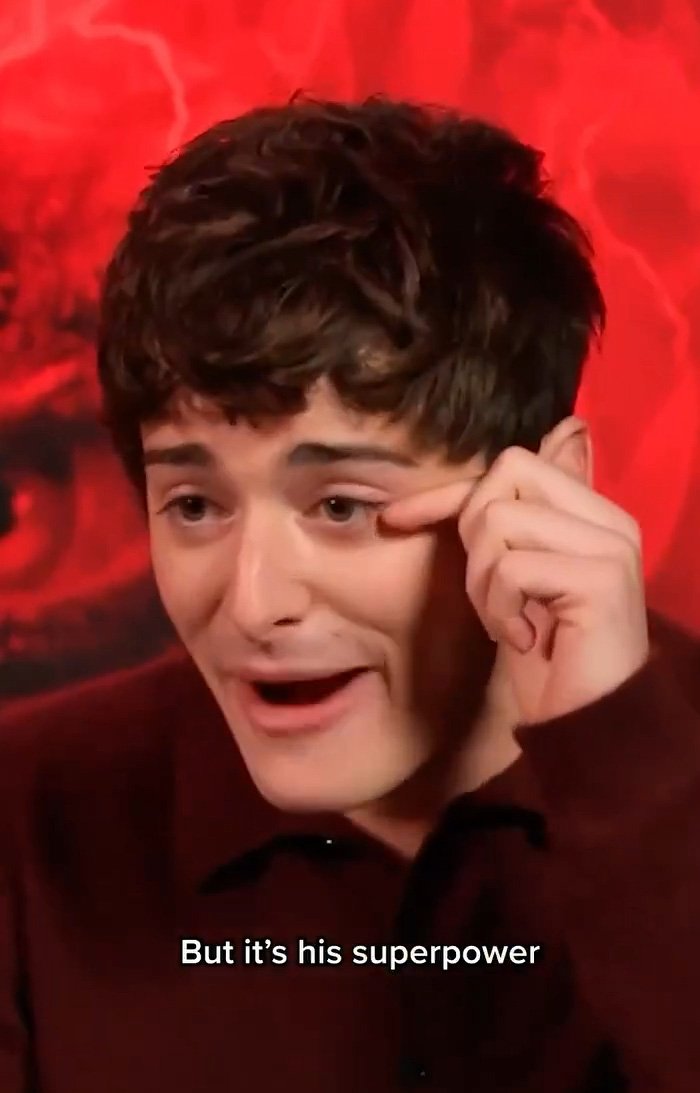 Noah Schnapp from Stranger Things speaking animatedly with a red background during an interview.