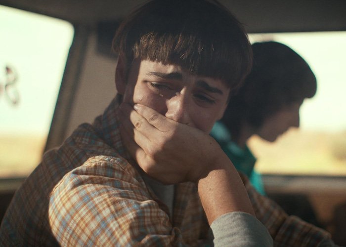 Noah Schnapp portraying Will Byers in Stranger Things, looking distressed inside a vehicle with another character blurred.