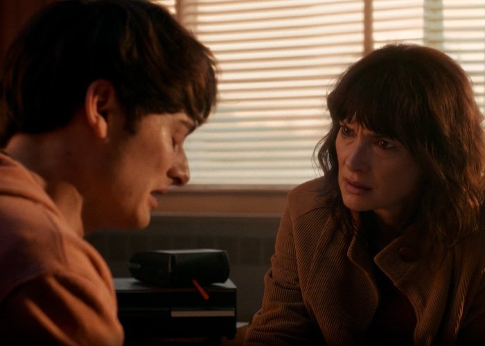 Two people having a serious conversation in a dimly lit room, relating to Stranger Things star Noah Schnapp.