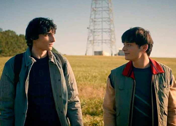 Stranger Things star Noah Schnapp and co-actor walking outdoors with a tower in the background during a scene.