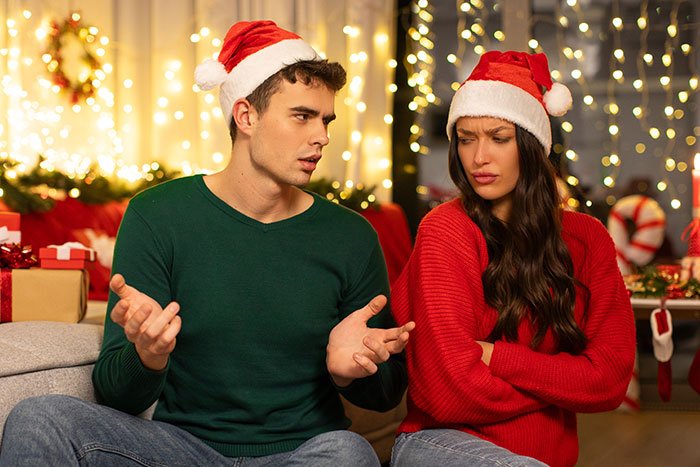 Woman confused about Christmas gifts from boyfriend, both wearing Santa hats, sitting amid festive holiday decorations.
